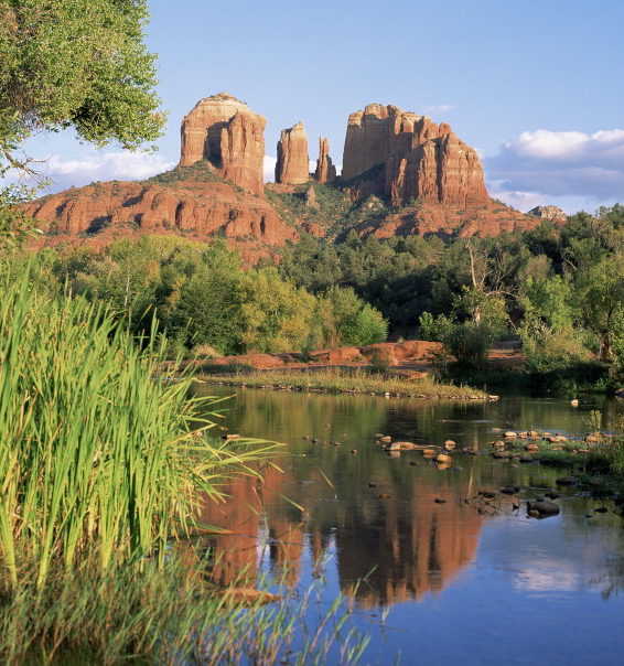 A blue lake and green vegetation sits at the base of the red rock formation: Cathedral Rock